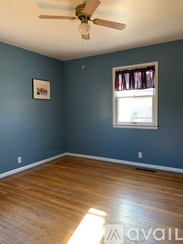 A room with a ceiling fan and a window with a picture hanging on the wall.