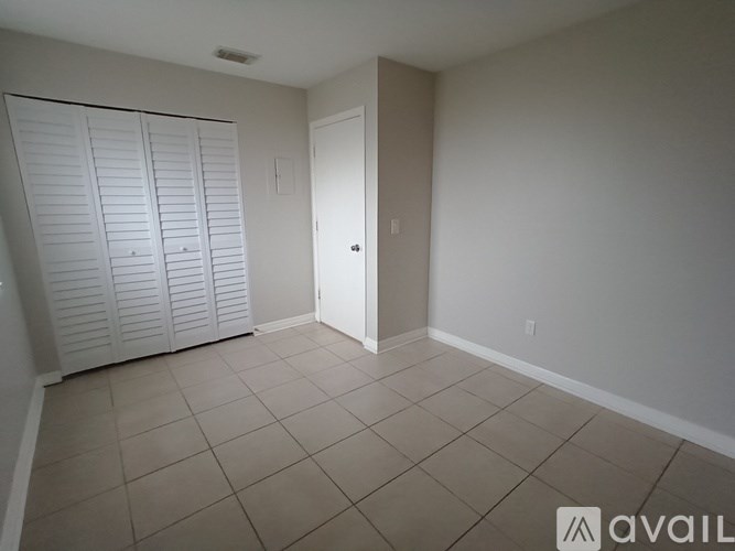 A room with white walls and a tiled floor with a door and a closet with white doors.