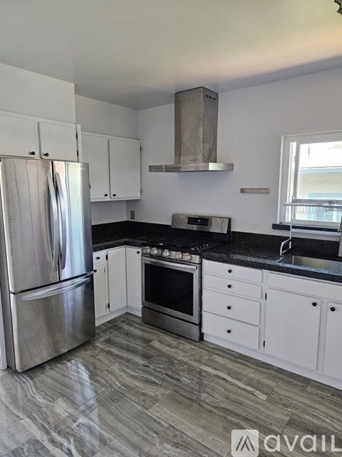 A kitchen with a stainless steel refrigerator and oven, white cabinets, and a black countertop.