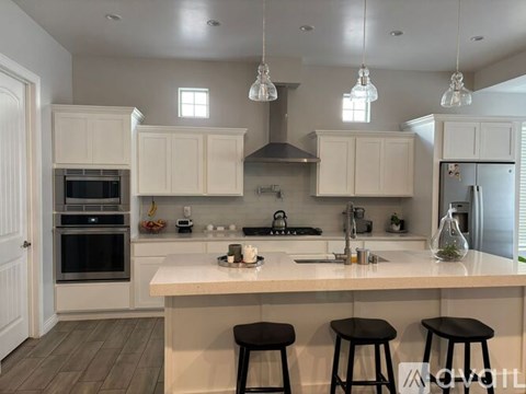 A kitchen with white cabinets and a large island with three stools.