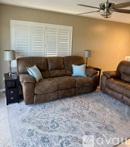 A living room with a brown couch, two lamps, and a ceiling fan.