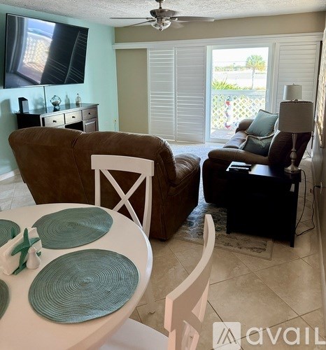 A living room with a brown couch, a white chair, and a television on the wall.