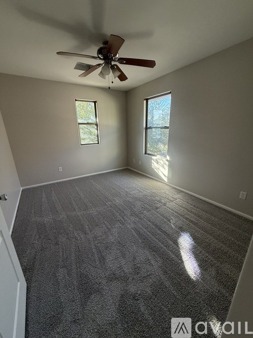 A room with a ceiling fan and two windows.