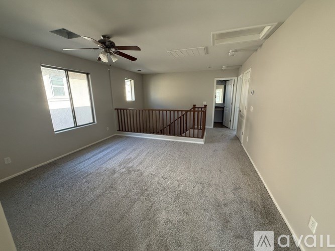 A spacious room with a carpeted floor, a ceiling fan, and a staircase with wooden railings.
