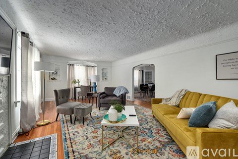 A living room with a yellow sofa and a rug with a coffee table in front of it.