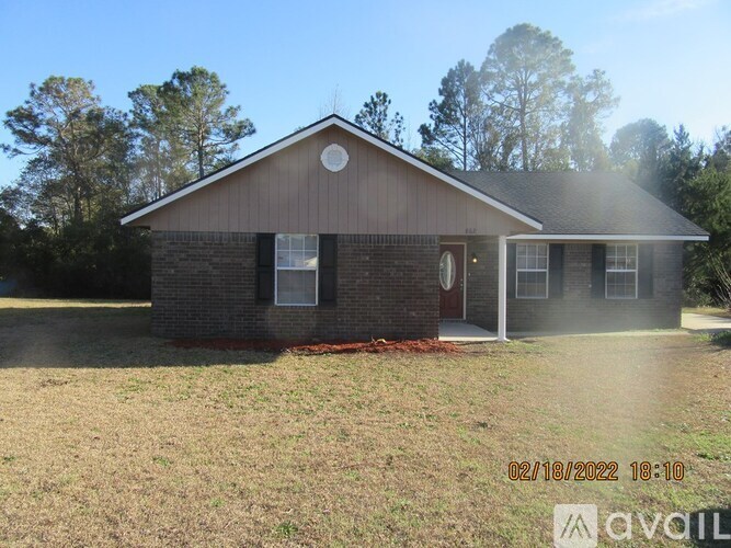 A house with a brown roof and a white door is surrounded by grass and trees.