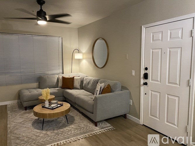 A living room with a grey couch, a round mirror, a coffee table, and a ceiling fan.