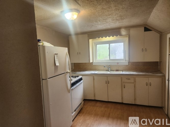 A kitchen with a white refrigerator, wooden cabinets, and a window.