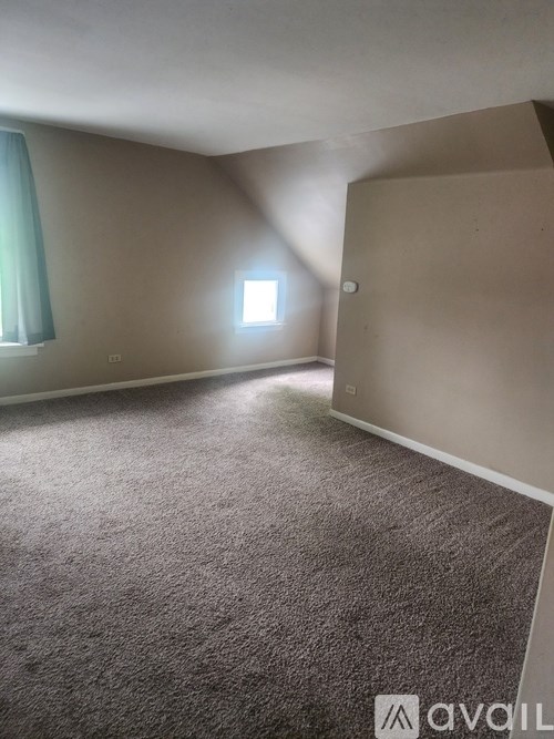 A carpeted room with a window and a wall-mounted light fixture.