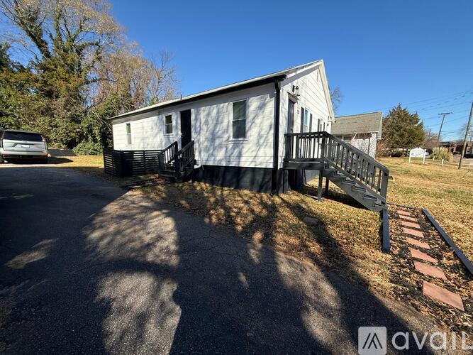 A small white house with a black fence and a black trash bin in front of it.