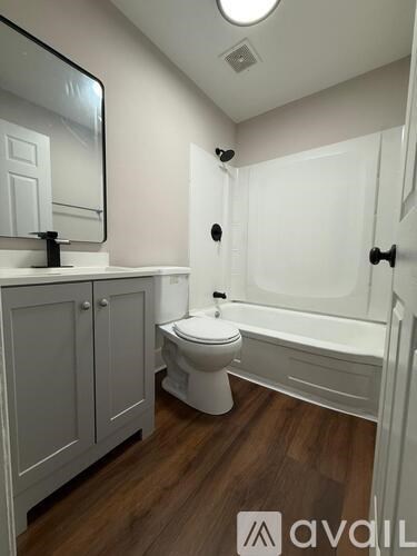 A white toilet in a bathroom with wooden floors and a white bathtub.