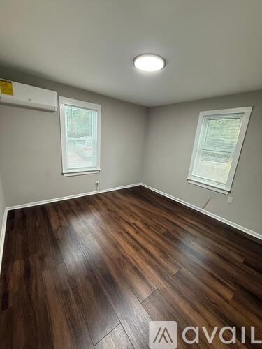 A room with wooden flooring and two windows.
