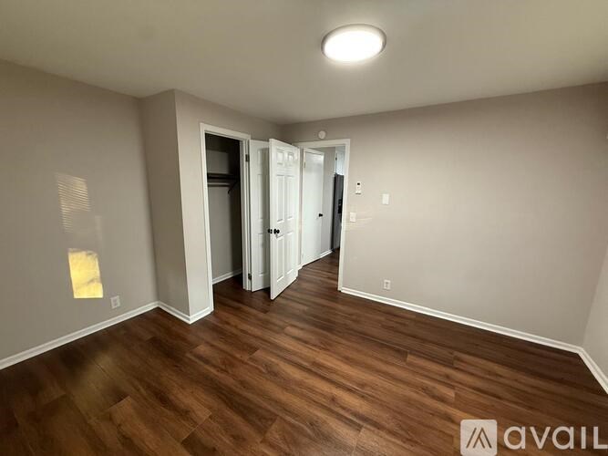 A room with wooden floors and white walls, with a doorway leading to another room.