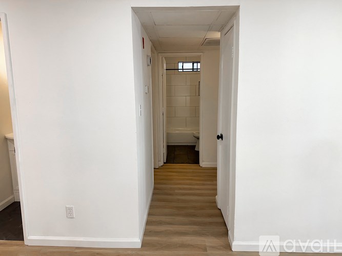 A long, narrow hallway with white walls and wooden flooring.