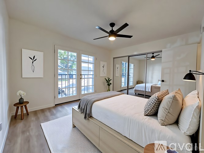A bedroom with a large bed, a ceiling fan, and a mirrored wall.