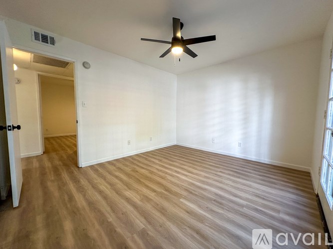 A spacious room with a ceiling fan and light, hardwood flooring, and a door leading to another room.