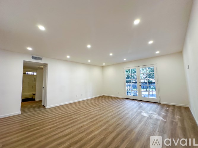A spacious room with wooden flooring and a window with blinds.
