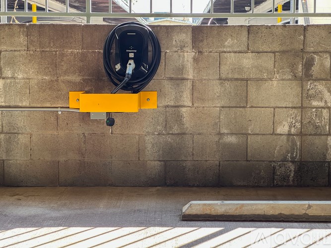 A black cable is plugged into a yellow outlet on a concrete wall.