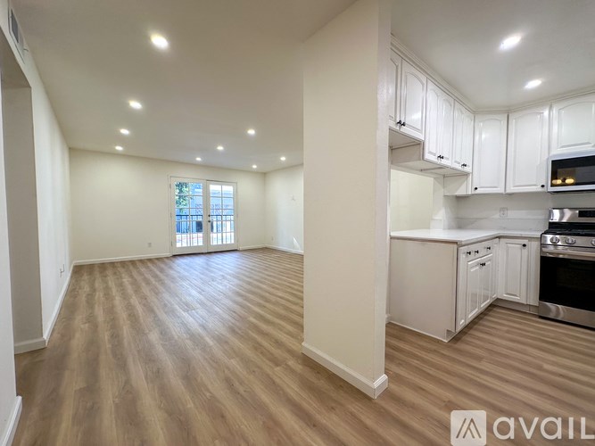 A spacious kitchen and living room with wooden floors and white cabinetry.