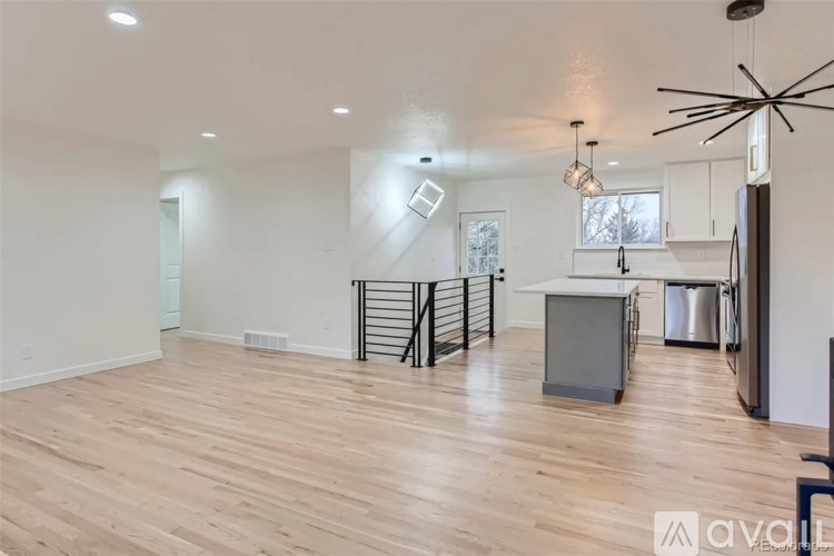 A spacious living room with wooden flooring and a kitchen area in the background.