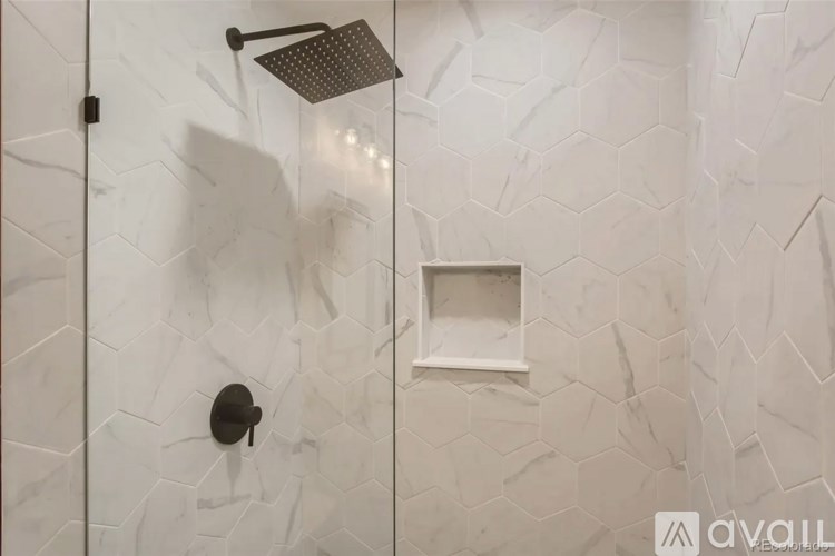 A shower with a white tiled wall and a square white tile on the wall.