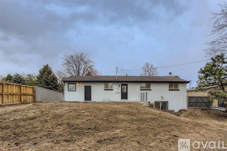 A house with a white exterior and a brown roof is surrounded by a wooden fence.