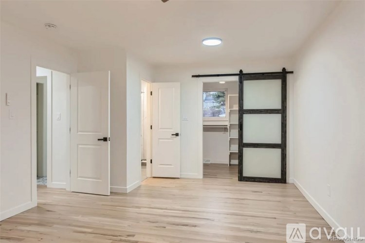 A spacious room with wooden flooring and white walls, featuring a black door with glass panels and a white door to the left.