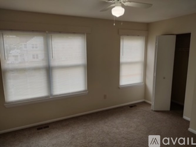 A room with a carpeted floor, a ceiling fan, and a window with blinds.