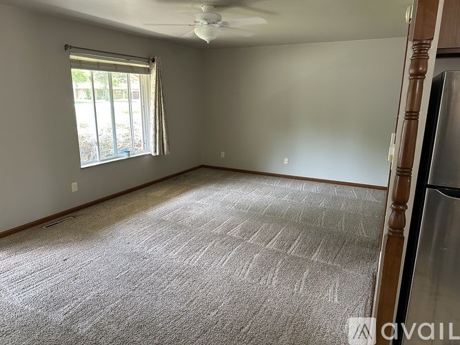 A room with a carpeted floor, a ceiling fan, and a window with blinds.