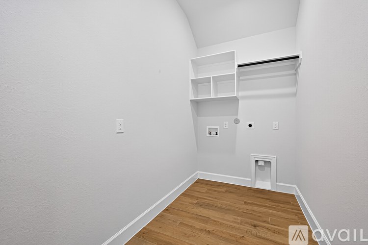 A room with white walls and wooden flooring, with a shelf and a vent on the wall.
