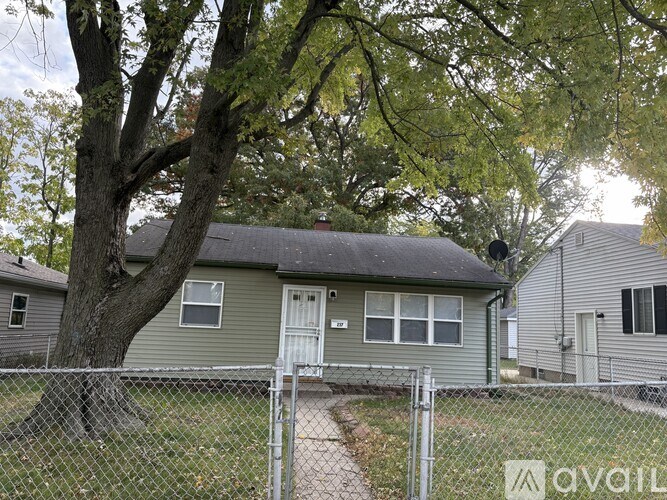 A house with a grey fence and a tree in front.