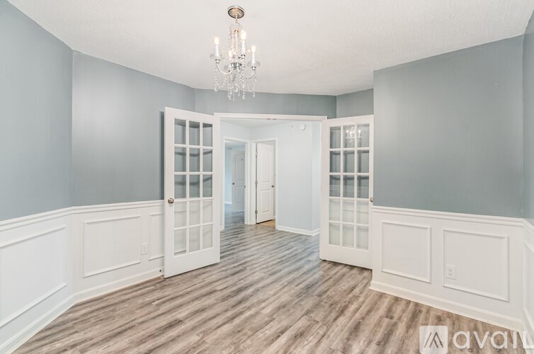 A room with a chandelier, wooden floors, and white doors.