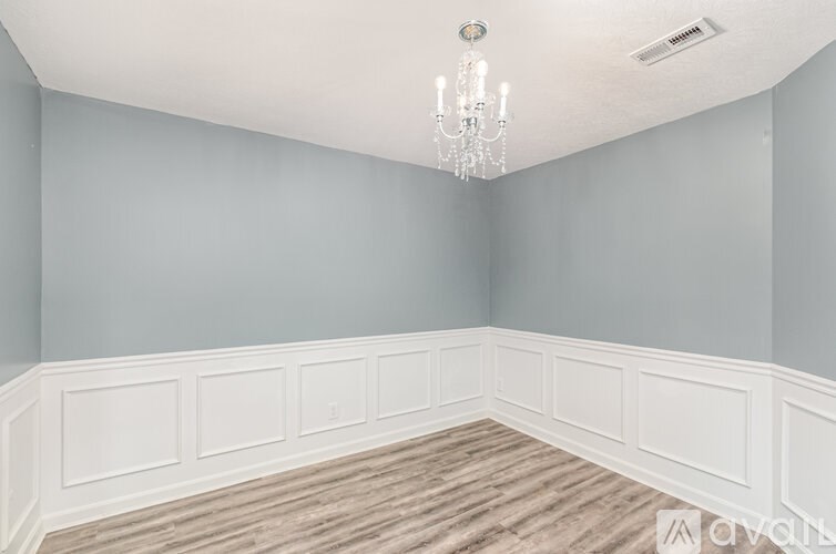 A room with a chandelier and white paneling on the walls.