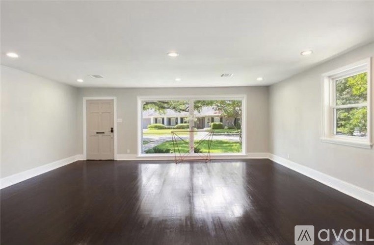 A spacious room with wooden floors and a view of a backyard through a large window.
