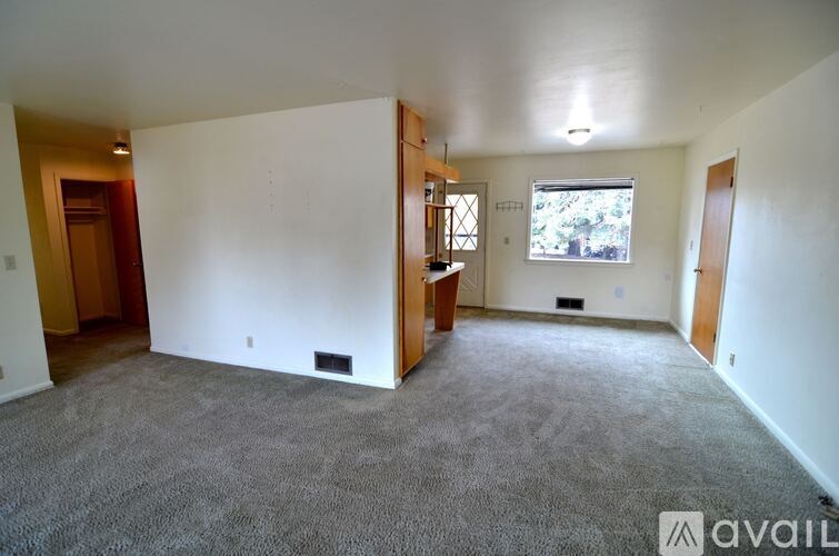 A room with a carpeted floor and a window with a view of trees outside.