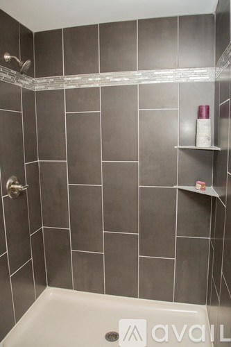 A bathroom with grey tiles and a white bathtub.