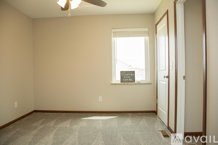 A room with a fan, carpet, and a window with a sign on it.