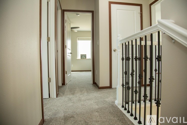A hallway with a carpeted floor and a staircase with a black railing.