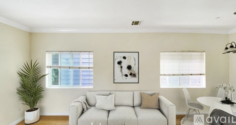 A living room with a white couch, a plant, and a painting on the wall.