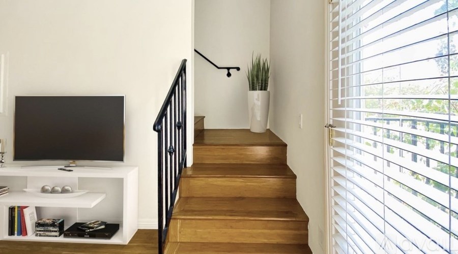 A staircase with a black railing and wooden steps leading to a window with white blinds.