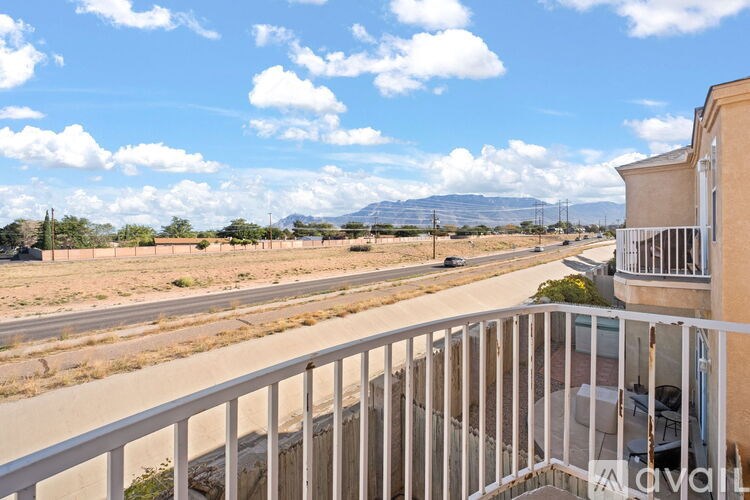 A balcony overlooks a road with a car and a landscape of trees and mountains.