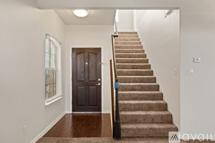A staircase with a brown carpeted runner and a black handrail leads up to a dark brown door.
