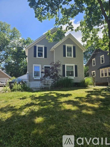 A house with a grey facade and white trim is surrounded by greenery.