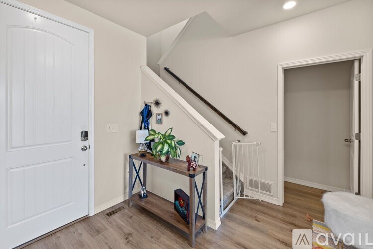 A white door is on the left of a room with a wooden floor and a staircase.
