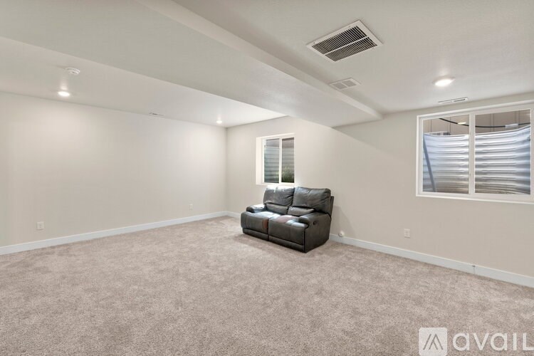 A spacious living room with a black leather sofa and a window with blinds.