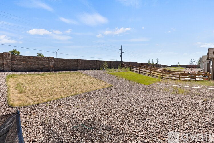 A gravel area with a grassy patch and a fence in the background.
