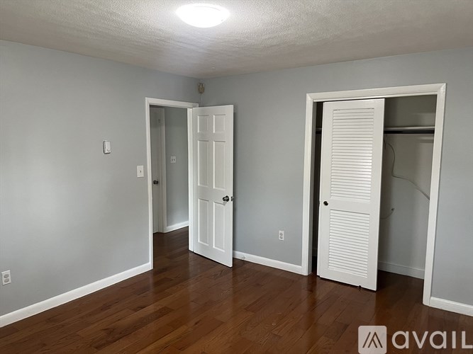 A room with white walls and wooden floors has two doors and a window.