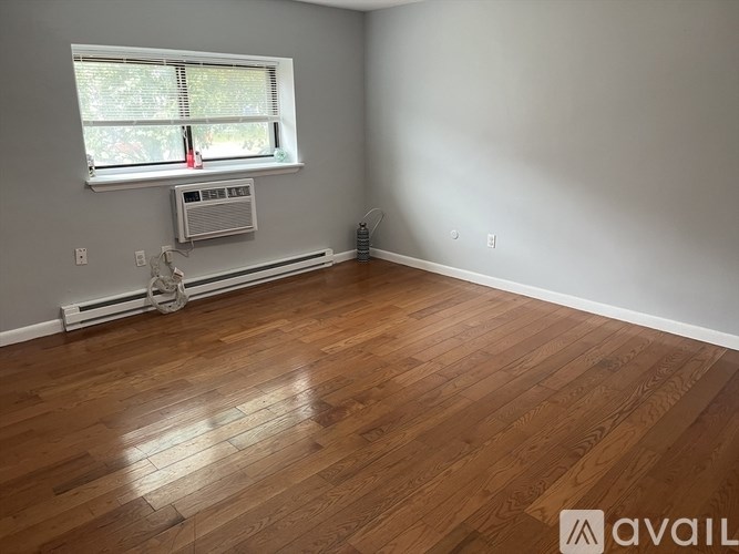 A room with wooden flooring and a window with an air conditioner underneath it.