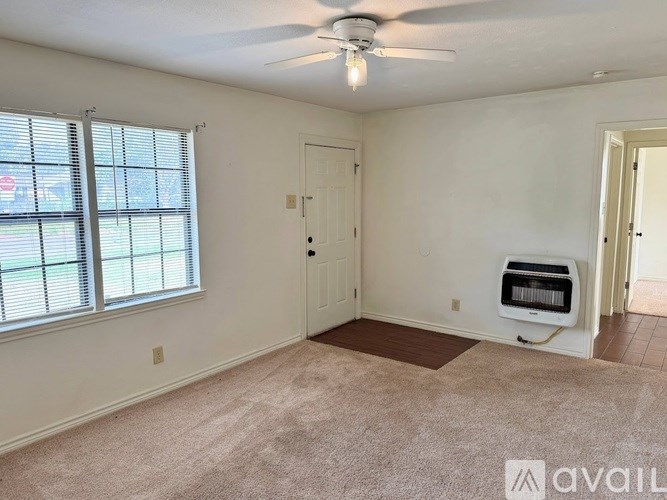 A room with a carpeted floor, a ceiling fan, and a window with blinds.