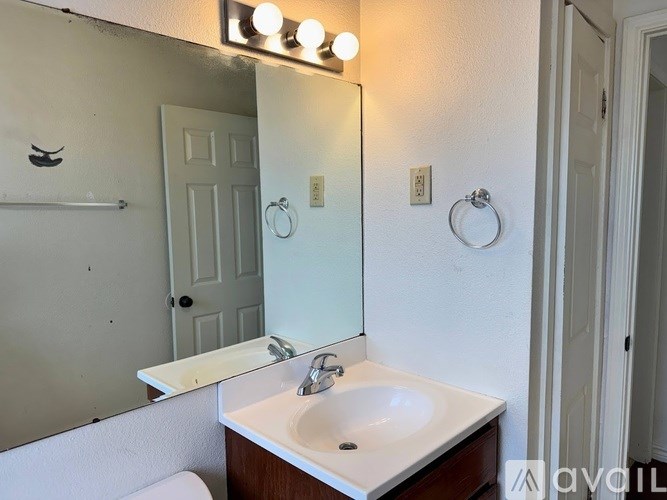 A bathroom with a white sink and a mirror with lights on it.